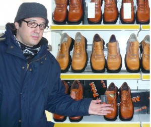 Image of a man wearing glasses and standing in front of shelves containing rows of men's shoes